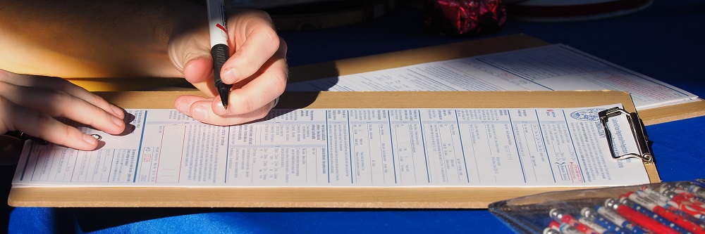 A picture of a hand with a pen over a voter registration form on a clipboard.