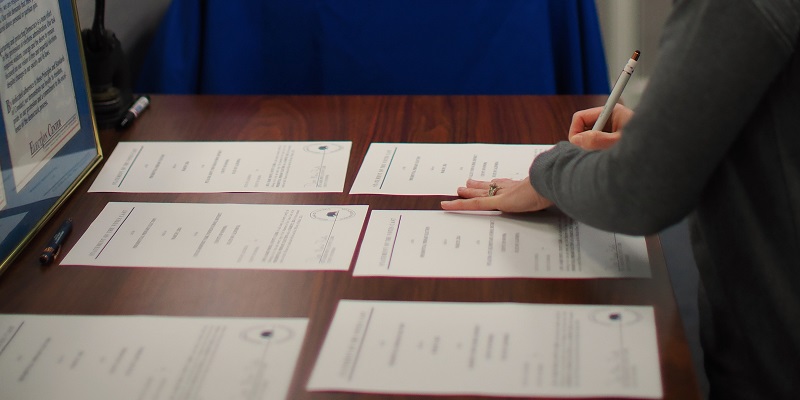 A picture of somebody's hand signing one of six pieces of paper laid out on a table